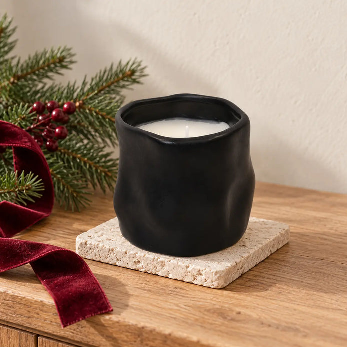 Unlit black sculpted vessel candle beside Christmas greenery and burgundy ribbon