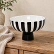 Black and white decorative footed bowl displayed empty on a rustic sideboard