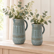 Blue ceramic jugs shown together for size comparison, large 32cm and medium 27cm, with white blossom and eucalyptus; sold separately.