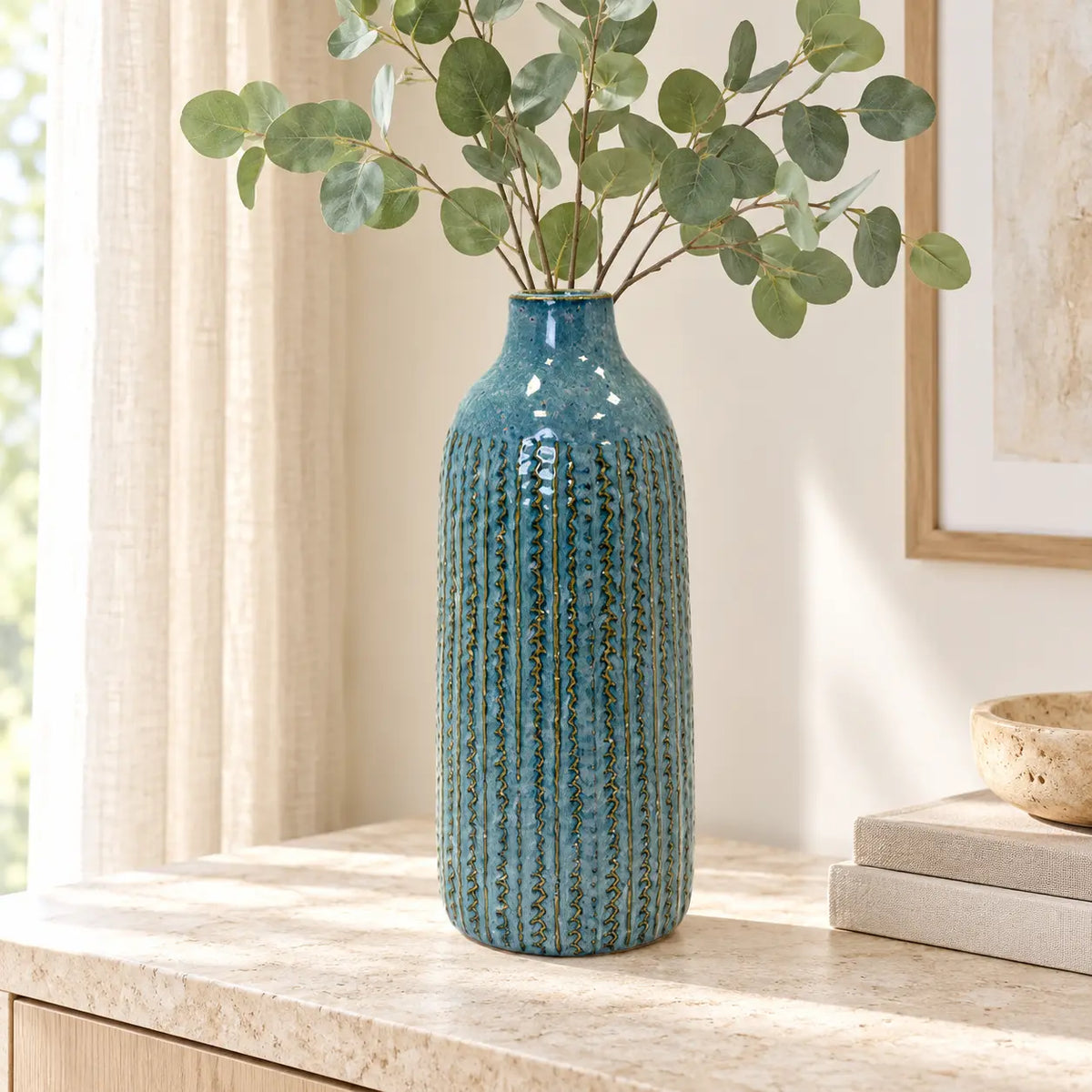 Large blue ceramic vase styled with eucalyptus on a light stone sideboard.