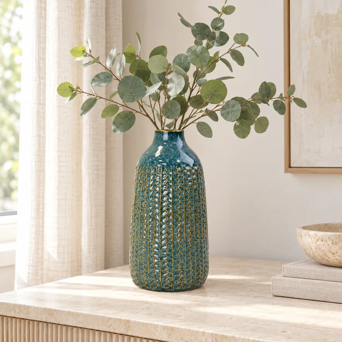 Medium blue ceramic vase styled with eucalyptus on a light stone sideboard.