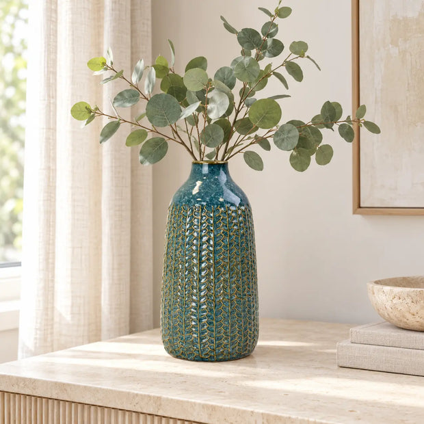 Medium blue ceramic vase styled with eucalyptus on a light stone sideboard.