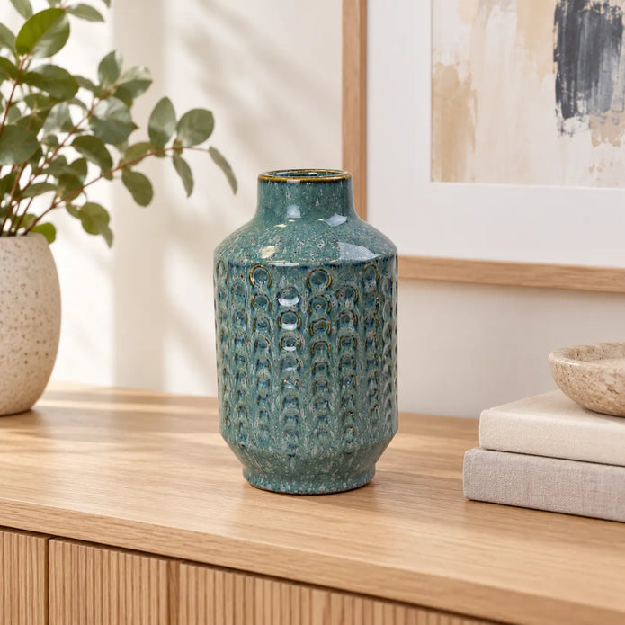 Small blue ceramic vase on an oak console in a bright neutral interior.