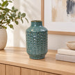 Small blue ceramic vase on an oak console in a bright neutral interior.