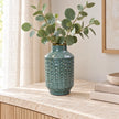 Small blue ceramic vase styled with eucalyptus on a light stone sideboard.