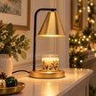 Black and brass-effect candle warmer lamp glowing above an unlit candle on a console