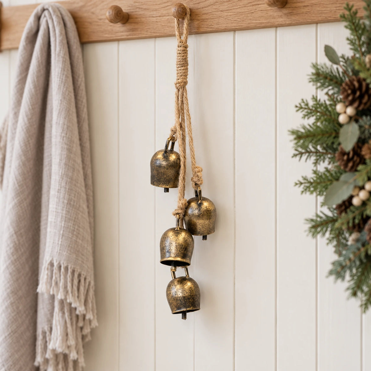 Brass-toned cowbell garland hanging from an oak peg rail in a Christmas hallway