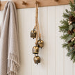 Brass-toned cowbell garland hanging from an oak peg rail in a Christmas hallway