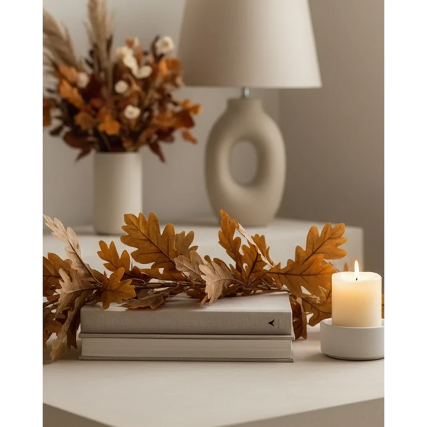 Brown Autumn Leaf Garland, brown leaves draped over books beside a candle and vase