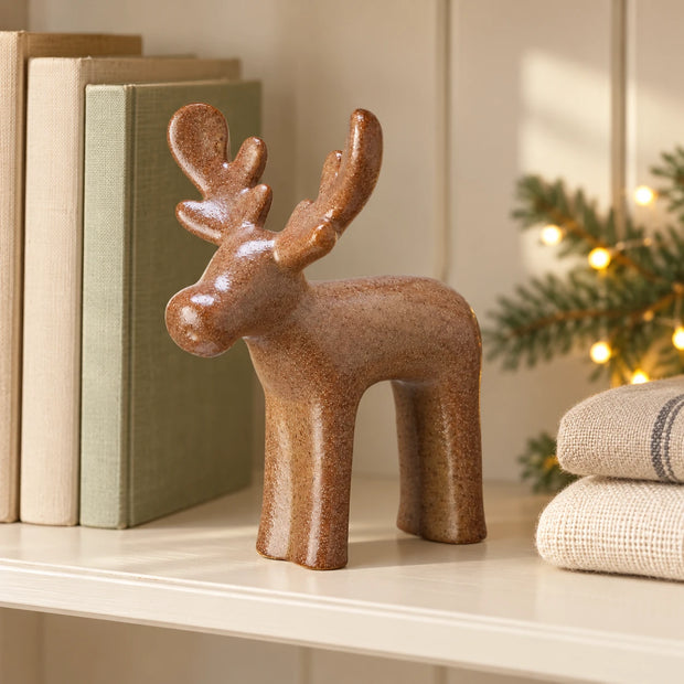 Brown Ceramic Reindeer — Single reindeer on cream bookshelf beside neutral books and folded linen