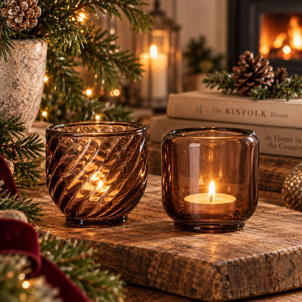 Two brown glass tealight holders, twisted patterned and smooth plain, styled with pinecones and festive candles