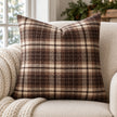 Brown and cream tartan cushion cover on an oatmeal armchair with a knitted throw