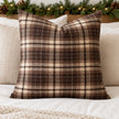 Brown tweed tartan cushion cover styled on ivory bedding with Christmas greenery
