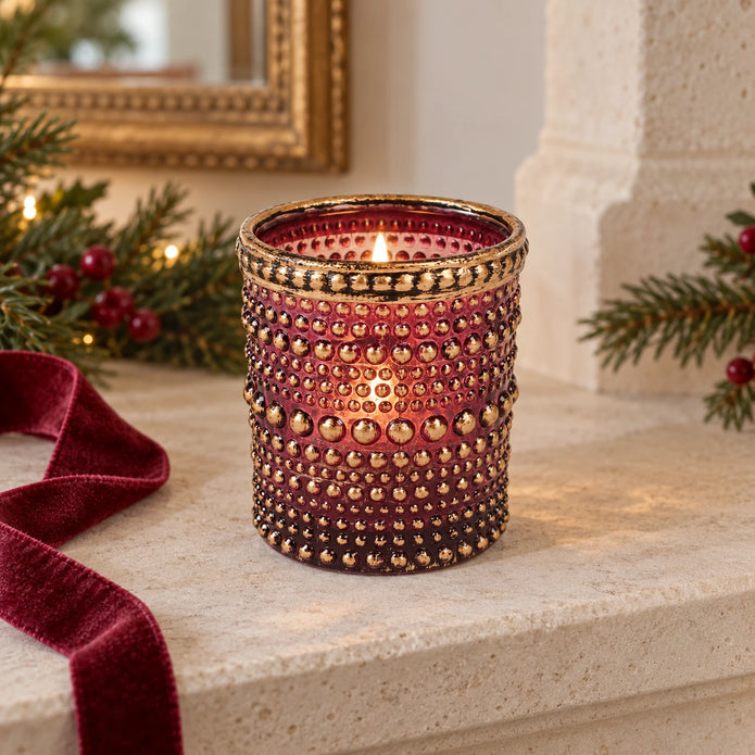 Burgundy dotted glass tealight holder with distressed gold rim, styled with a candle on a stone mantel.