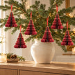 Six burgundy paper tree decorations with gold edges hanging from fir branches above an oak console.