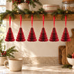 Six burgundy paper tree ornaments hanging from a festive kitchen shelf above a mug of tea.