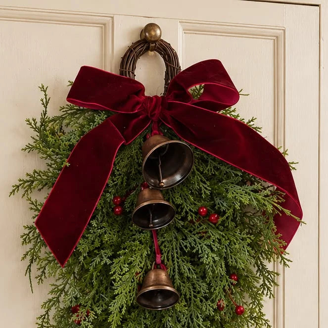 Christmas greenery swag with a burgundy bow and hanging bells on a door