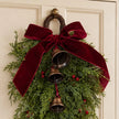 Christmas greenery swag with a burgundy bow and hanging bells on a door
