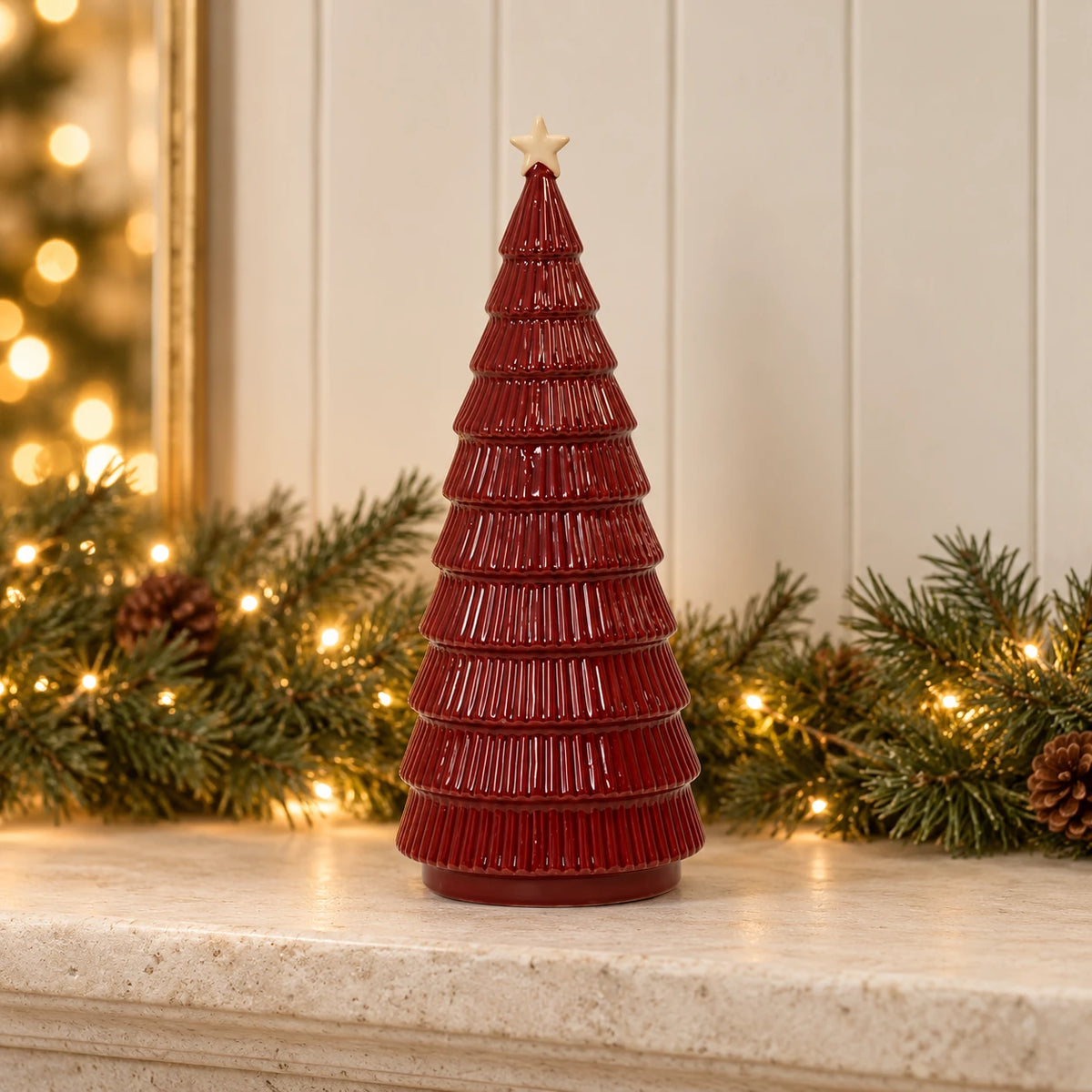 Burgundy ceramic Christmas tree styled on limestone mantel with pine garland