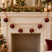 Six-bell burgundy metal garland hanging across a Christmas fireplace mantel