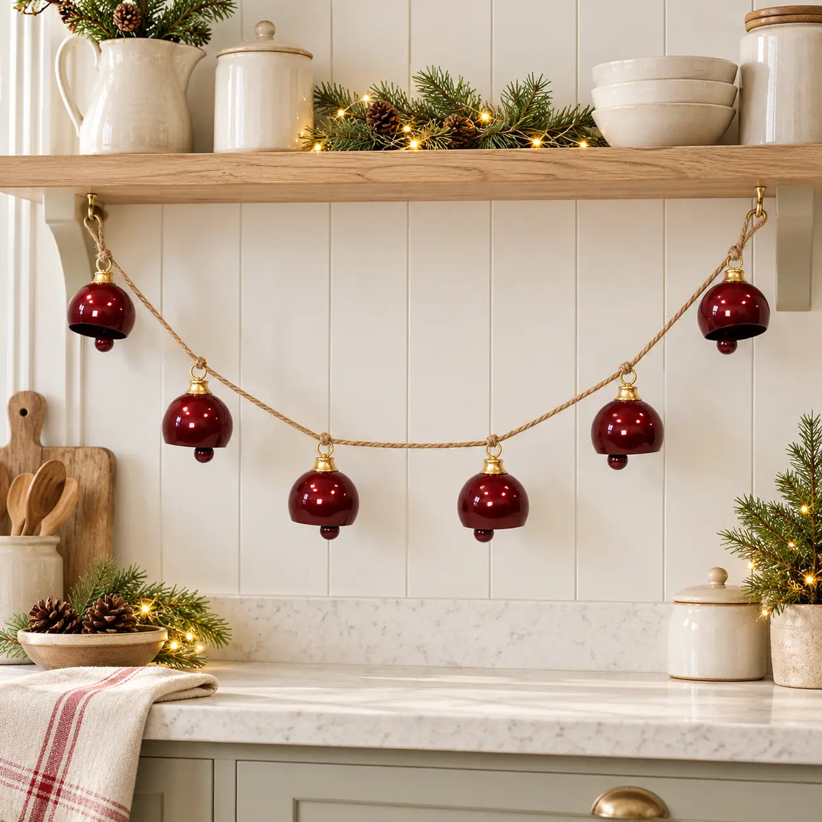 Burgundy metal bell garland beneath an oak shelf in a Christmas country kitchen
