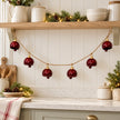 Burgundy metal bell garland beneath an oak shelf in a Christmas country kitchen