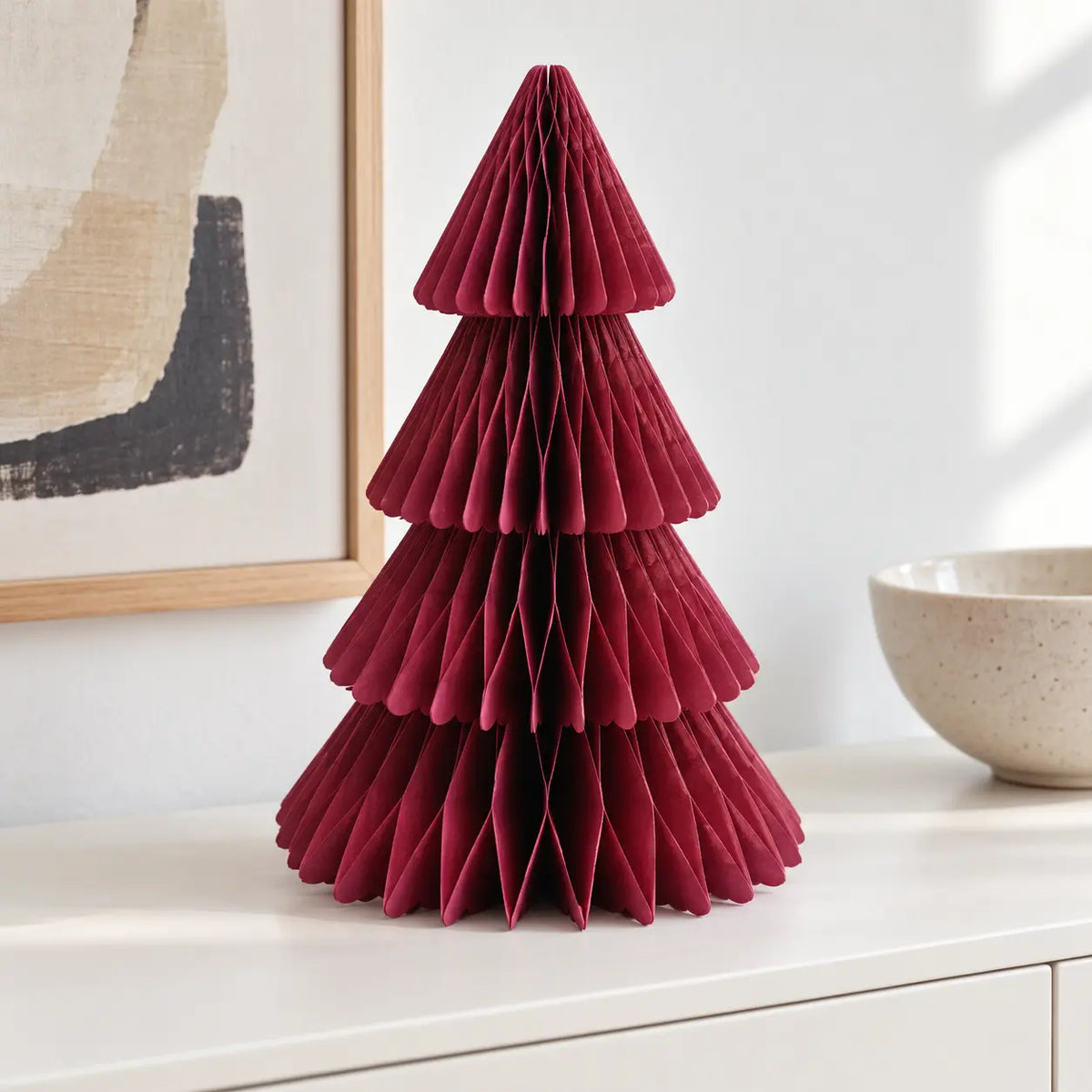 Claret red paper Christmas tree displayed on a white sideboard in daylight.