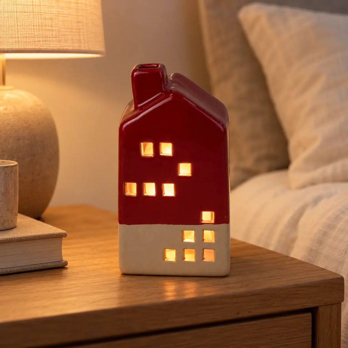 Burgundy red ceramic LED house glowing on a bedside table in an everyday interior.