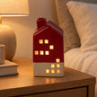 Burgundy red ceramic LED house glowing on a bedside table in an everyday interior.