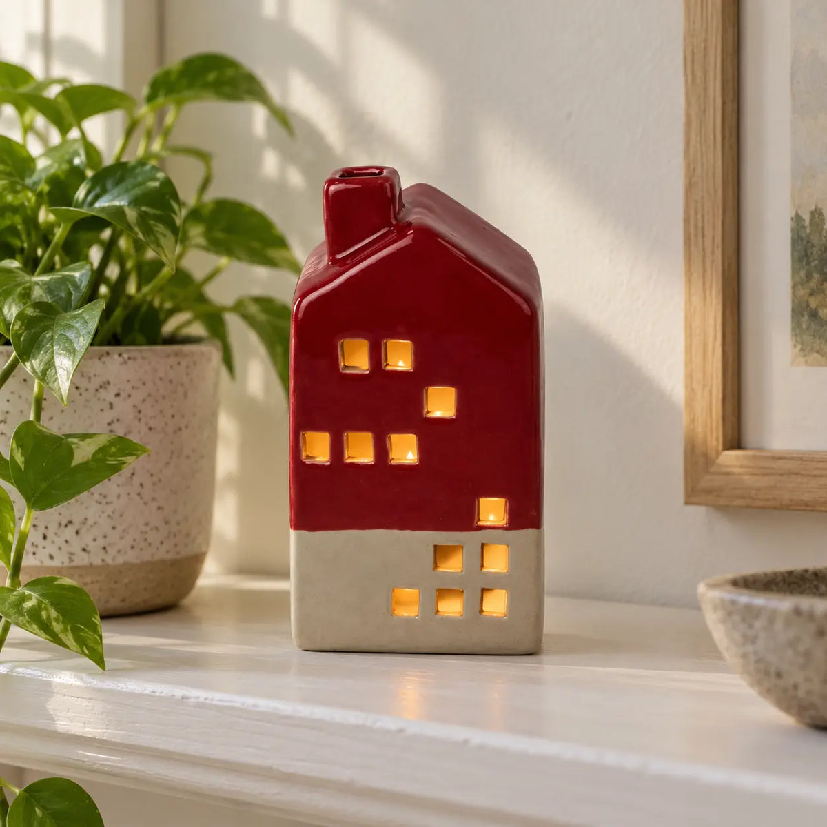 Burgundy red and cream ceramic LED house illuminated on a neutral shelf beside a plant.