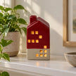 Burgundy red and cream ceramic LED house illuminated on a neutral shelf beside a plant.