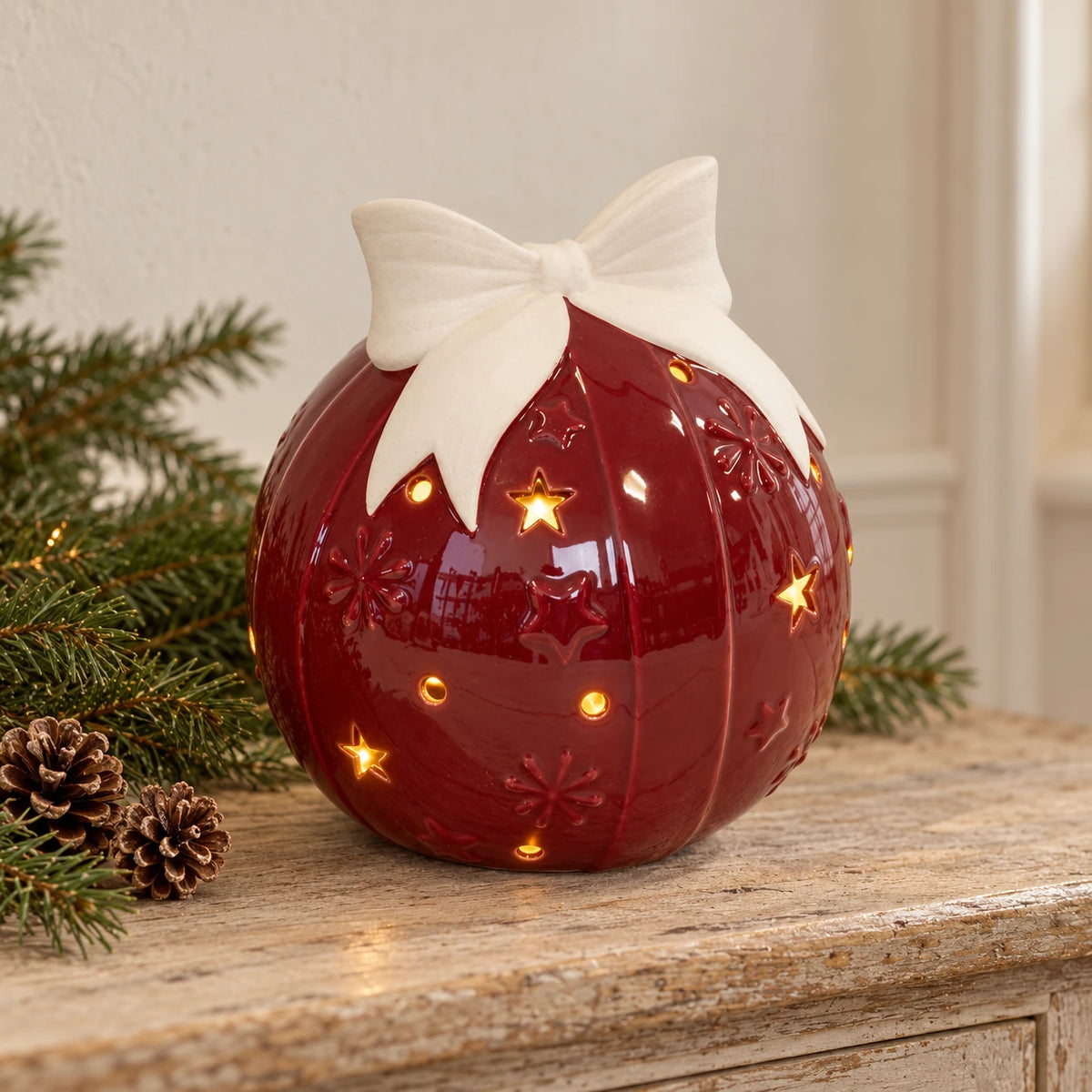 Burgundy red LED ceramic bauble with ivory bow on an oak console with Christmas greenery