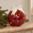 Burgundy red LED ceramic bauble with ivory bow on an oak console with Christmas greenery