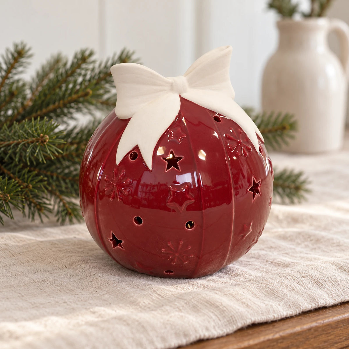 Burgundy red ceramic bauble with ivory bow on a linen Christmas sideboard