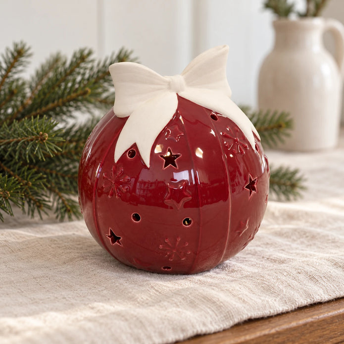 Burgundy red ceramic bauble with ivory bow on a linen Christmas sideboard