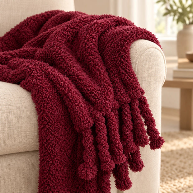 Burgundy Sherpa Tasselled Blanket Throw, close-up of the burgundy sherpa texture and tassels on a sofa arm