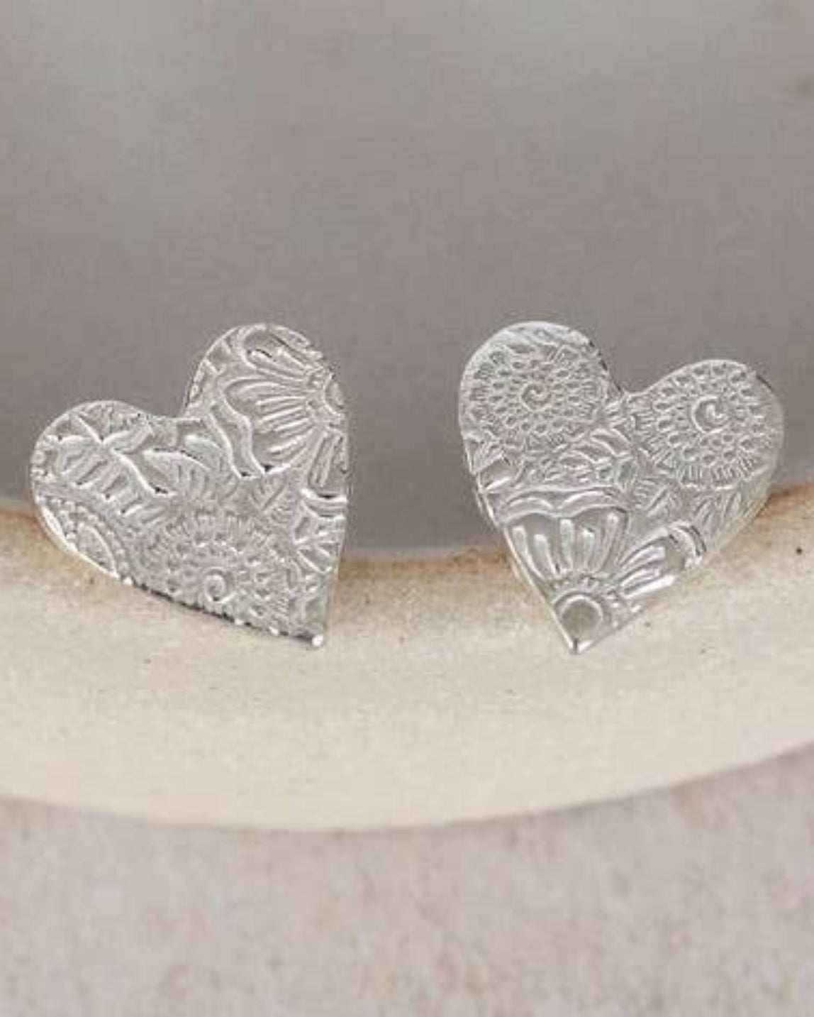 Silver heart-shaped earrings on a white ceramic dish