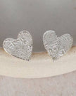 Silver heart-shaped earrings on a white ceramic dish