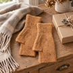 Camel speckle fingerless gloves arranged on a rustic oak table