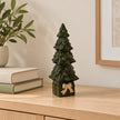 Dark green ceramic Christmas tree on a gift-shaped base with cream bow, on an oak console.