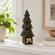 Green ceramic Christmas tree on box displayed on a white shelf in daylight.