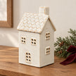 Unlit cream ceramic house tealight holder with tiled roof on a Christmas console