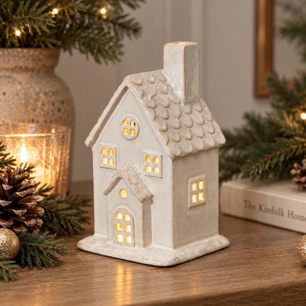 Large ceramic Christmas house with tall chimney and illuminated windows styled on a rustic console