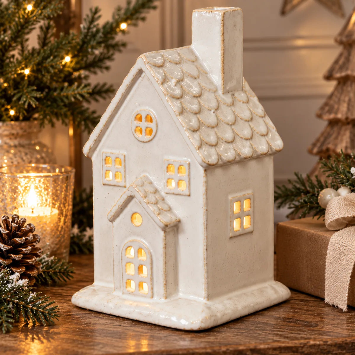 Close-up festive styling of large ivory ceramic house with textured roof and warm window glow
