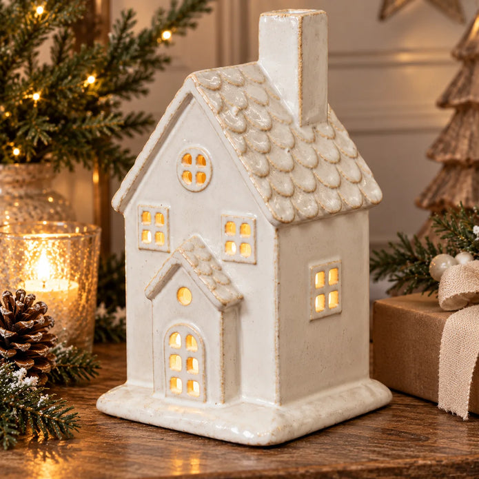 Close-up festive styling of large ivory ceramic house with textured roof and warm window glow