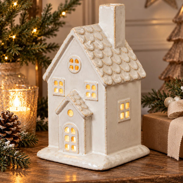 Close-up festive styling of large ivory ceramic house with textured roof and warm window glow