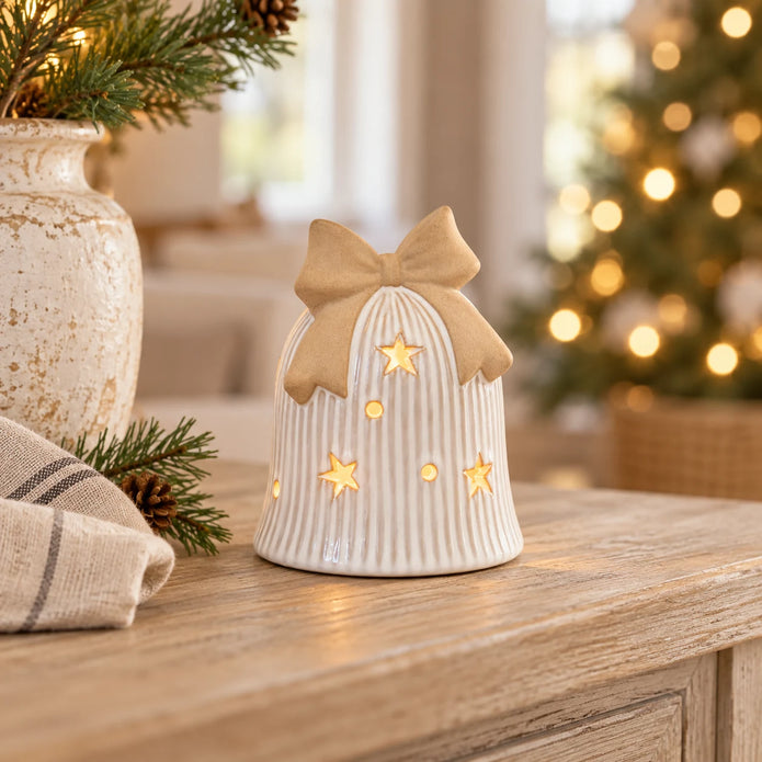 Ceramic LED Christmas bell with beige bow glowing on a light oak console