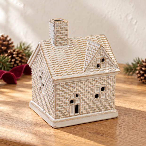 Ceramic cottage house switched off beside pinecones and burgundy ribbon