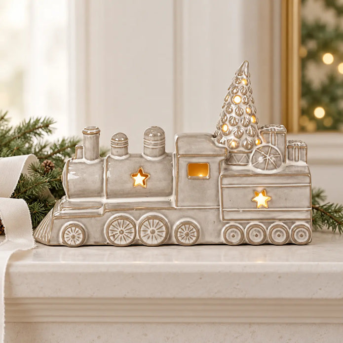 Glazed ceramic LED Christmas train on a pale mantel with fir greenery and white ribbon