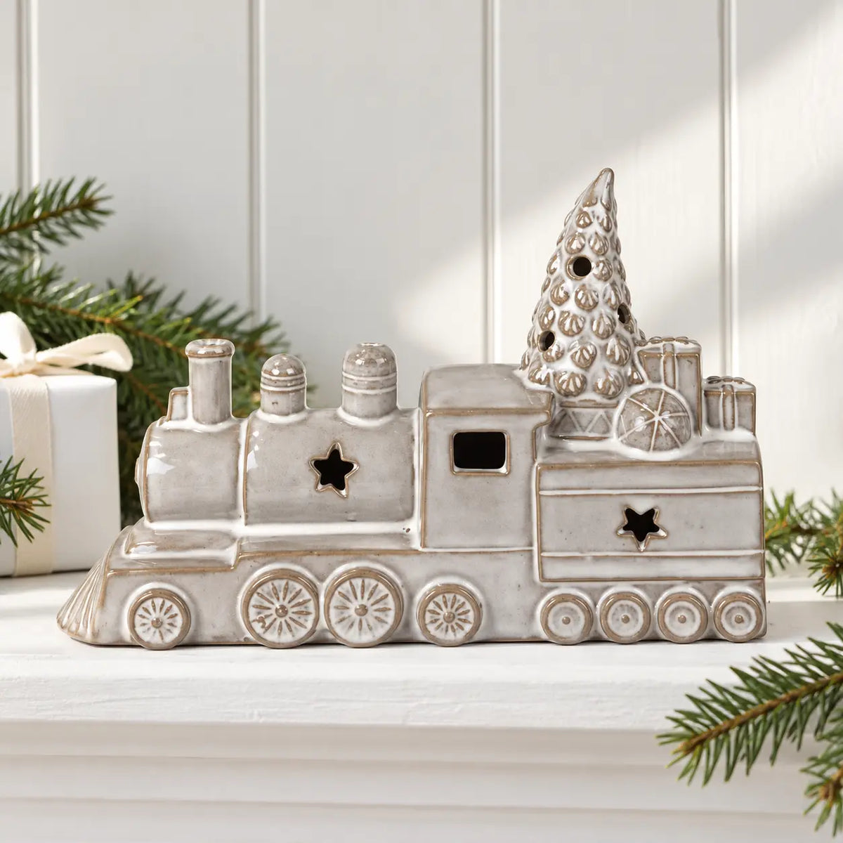 Grey glazed ceramic Christmas train on a white shelf with festive greenery